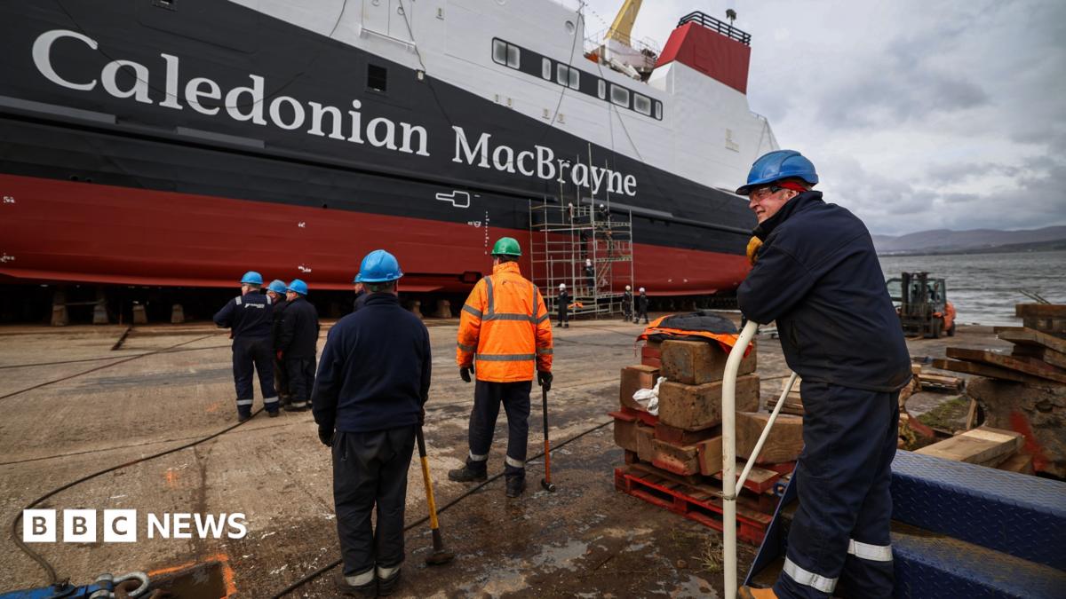 Workers make final preparations ahead of the launch of the MV Glen Rosa in April 2024. Six workers can be seen in the foreground with their back to the camera. The white, black and red ferry, with Caledonian MacBrayne written on the side, is in the distance.