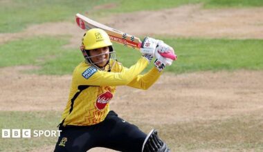 Sophia Dunkley, wearing a yellow helmet and shirt, plays a shot with her bat over her left shoulder