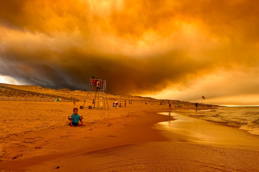 A landscape photo of a beach with dark orange skies.