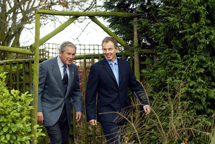 Two men walk under an archway.