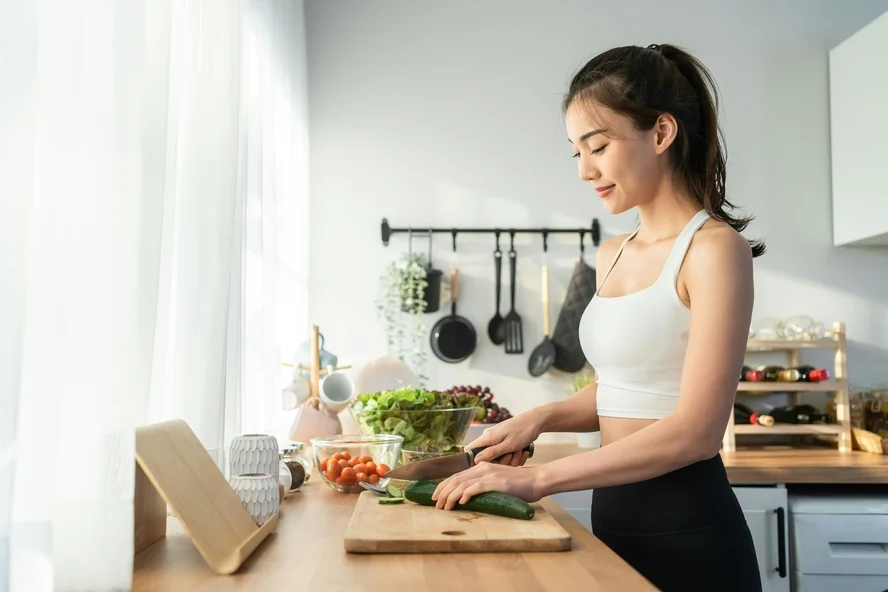 Image of a woman in a kitchen standing at the counter chopping some vegetables on a cutting board.