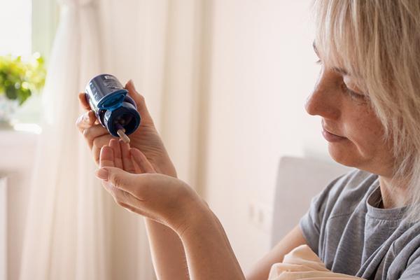 A middle-age woman holds a blue flip-top bottle and tips out capsules into her hand.