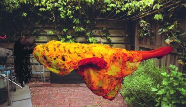 a photograph by Atong Atem of a woman wearing a warm-hued floral dress levitating as she lays horzontally