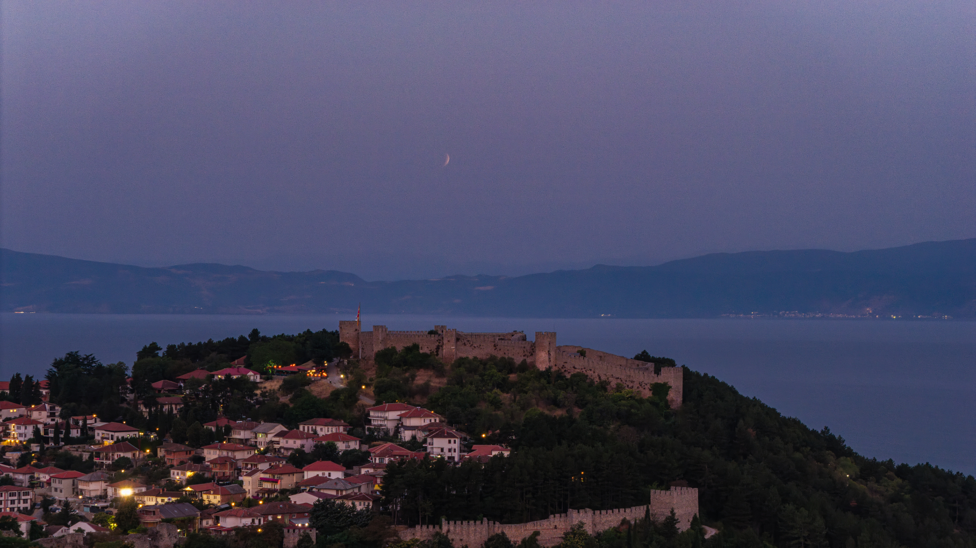 early morning sky with a partially eclipsed moon above the city and large lake below.