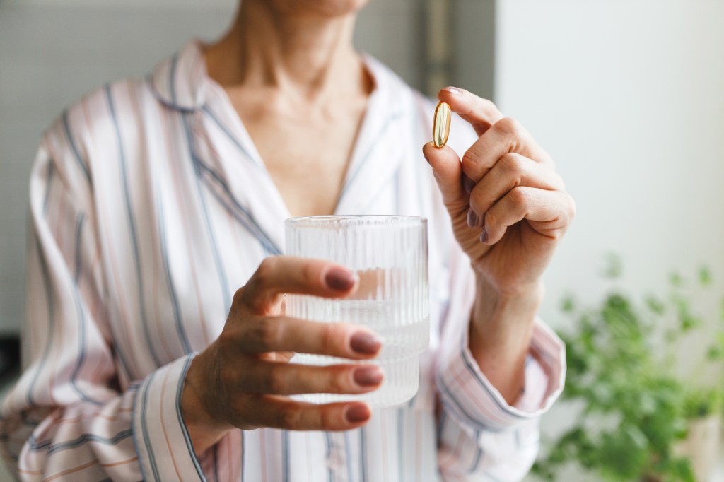 Woman holding a glass of water and a vitamin D3 or fish oil pill.