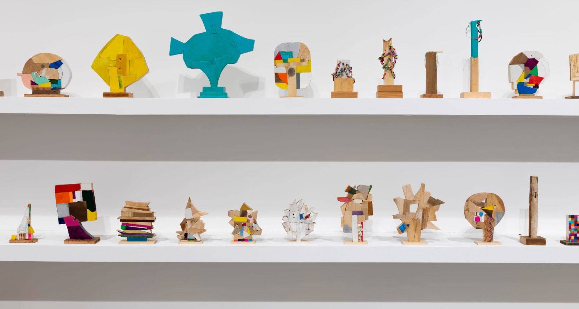 a collection of small abstract wooden sculptures painted in vibrant colors by damien hoar de galvin on white shelves