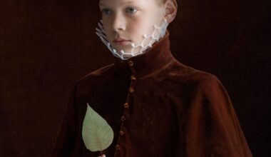 a portrait by Suzanne Jongmans of a young boy wearing a velvet jacket, with a neck ruff made of plastic used to protect fruit, holding a green leaf