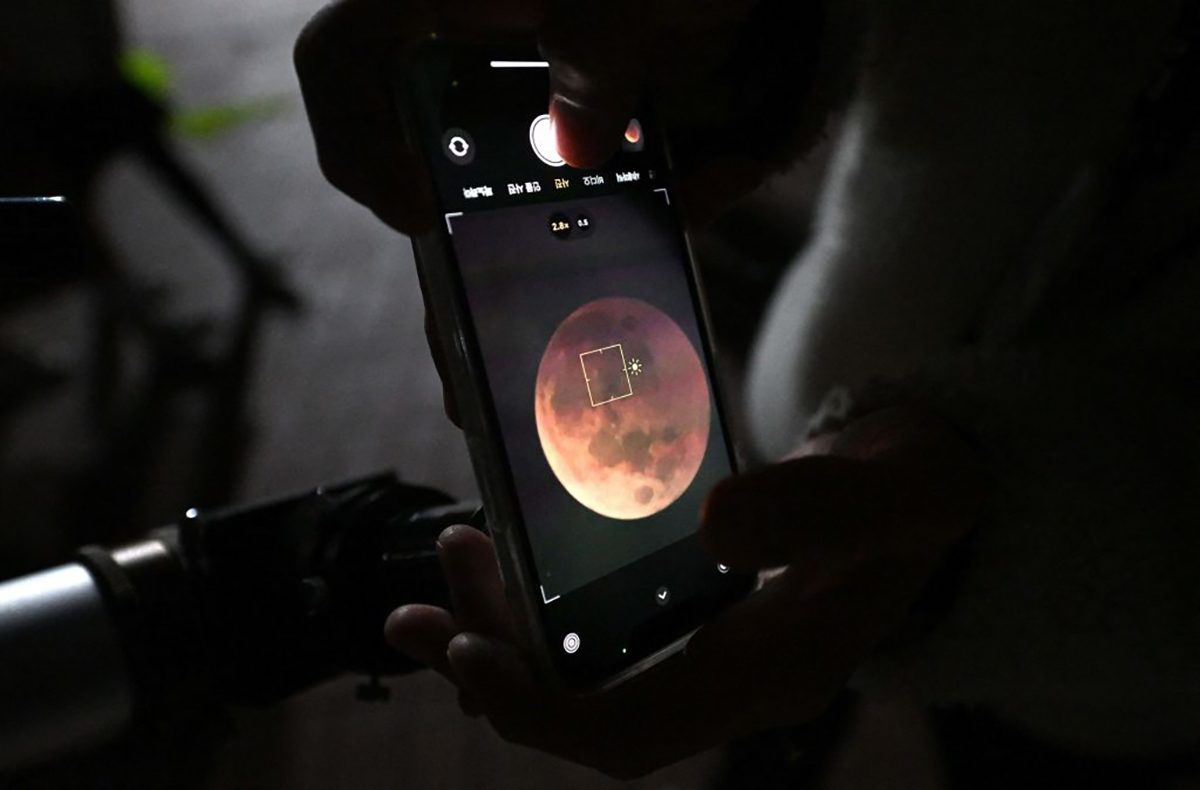 A man uses a smartphone to take picture of a blood moon through telescope during a total lunar eclipse in Goyang, northwest of Seoul, on November 8, 2022. (Photo by JUNG YEON-JE / AFP) (Photo by JUNG YEON-JE/AFP via Getty Images