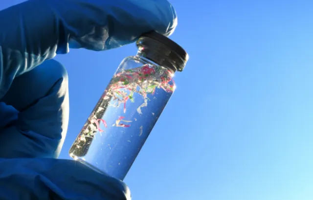 Gloved hand holding a small bottle containing microplastics
