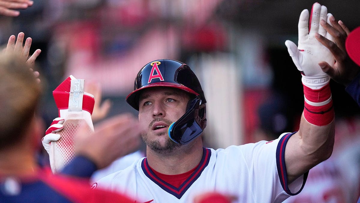 Mike Trout stands in the dugout as teammates congratulate him after he scores.