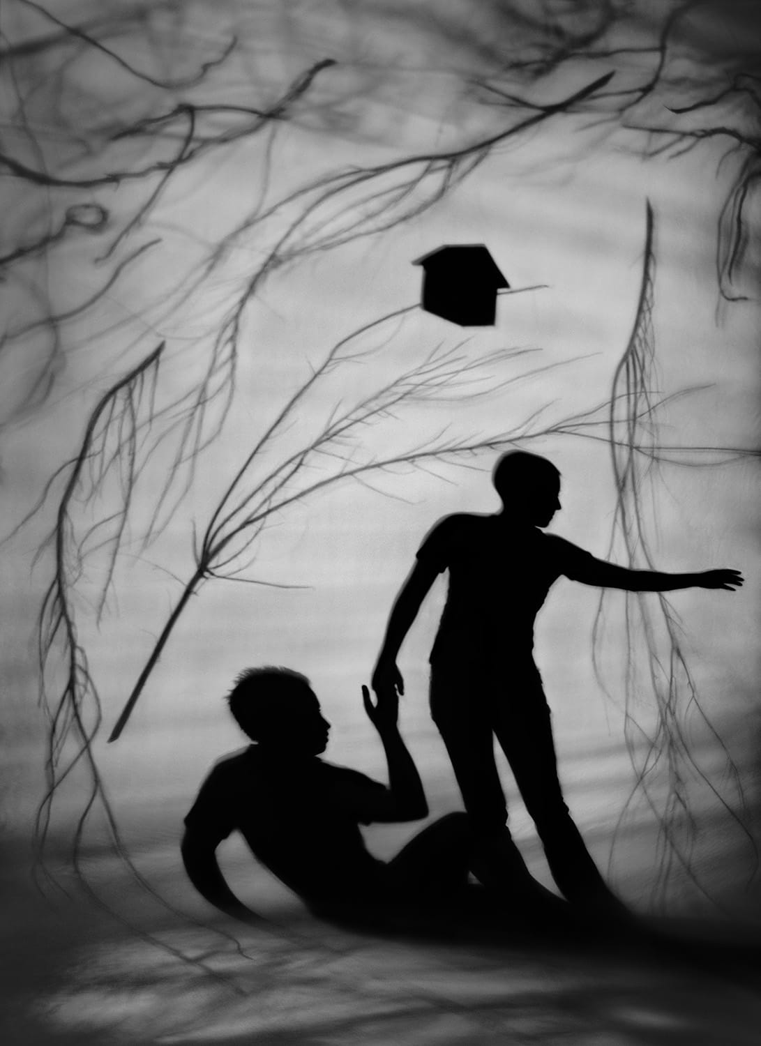 a black-and-white photograph by Susan kae Grant of a silhouetted dream-like scene of two figures struggling to move in a windy situation with branches flying around and a tiny house in the air