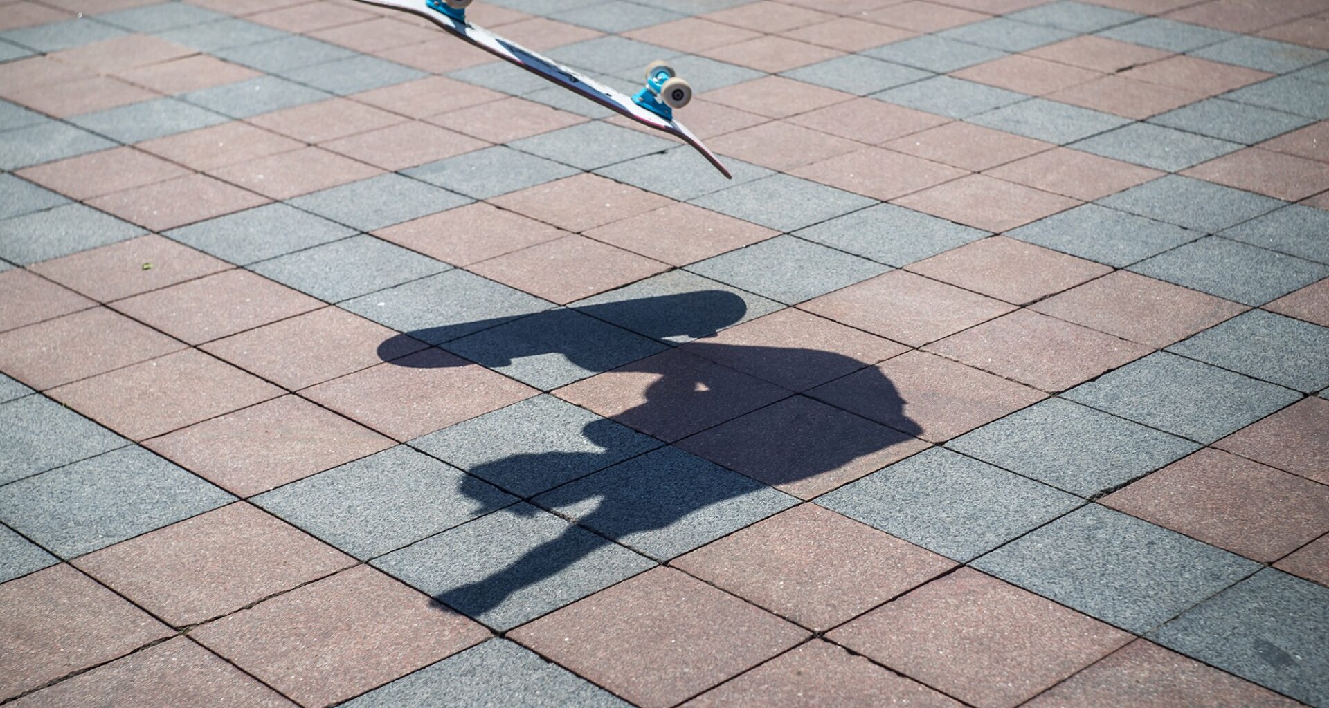 a street photo of a skateboard mid-air with the shadow of the skateboarder below