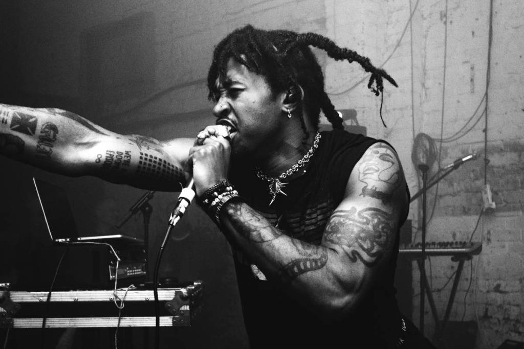 a black and white photo of musician FREDDY FORBIDDEN singing into a microphone at a gig