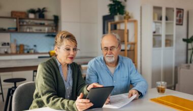 Senior couple sitting at a table and talking while looking at a tablet screen.