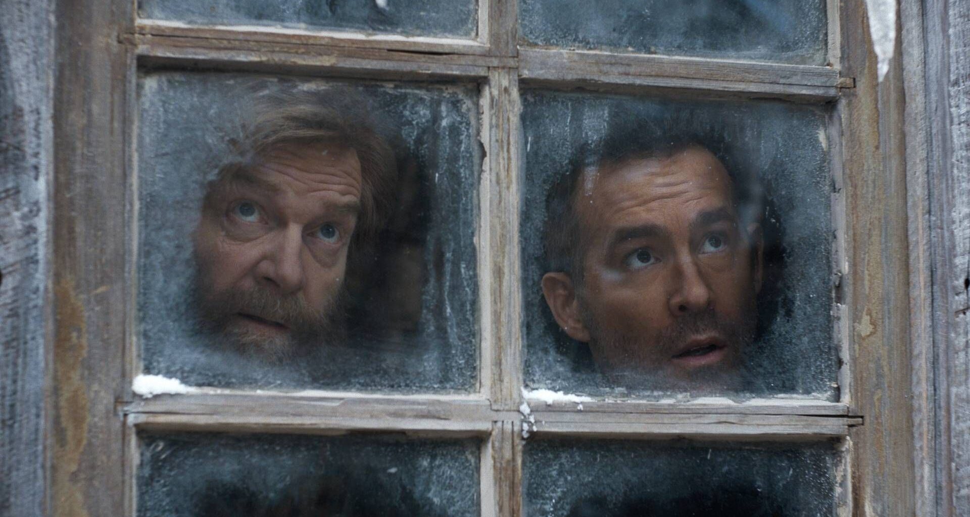 L to R: Kenneth Branagh as Nikolai Ustinov and Ryan Reynolds as Troy Kelly looking out of a frosted windown in Mayday