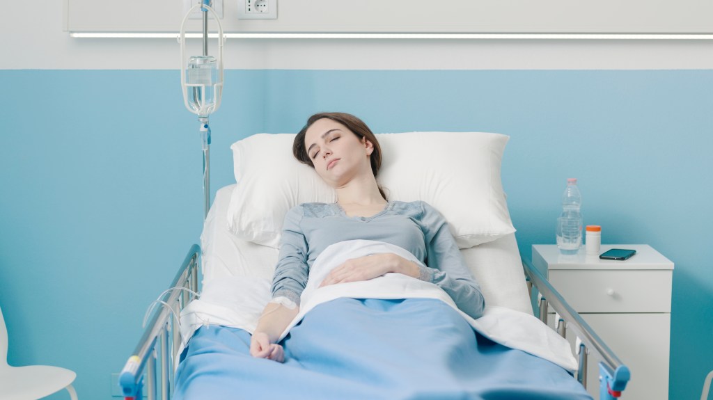 A young female patient lies in a hospital bed with an IV drip.
