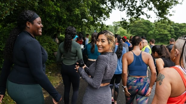An over the shoulder view of a large group of people who are taking part in an inclusive race which is open to all ages and abilities and even open to dogs. They are all walking toward the starting line after doing some warm up exercises in a group.