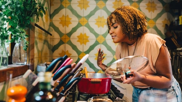Woman smiling with her eyes closed while smelling food cooking in a pot on a stove in her kitchen at home