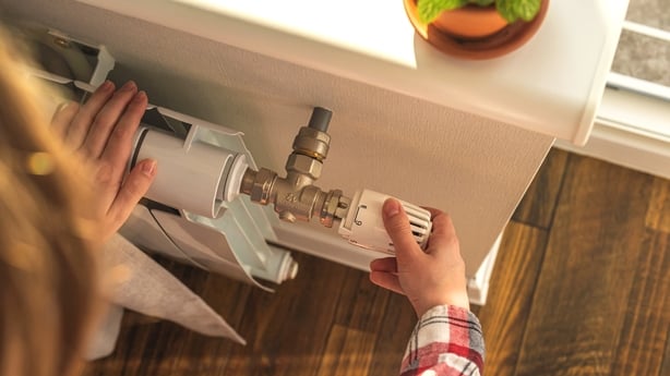 Woman adjusting the temperature on valve of a radiator at home