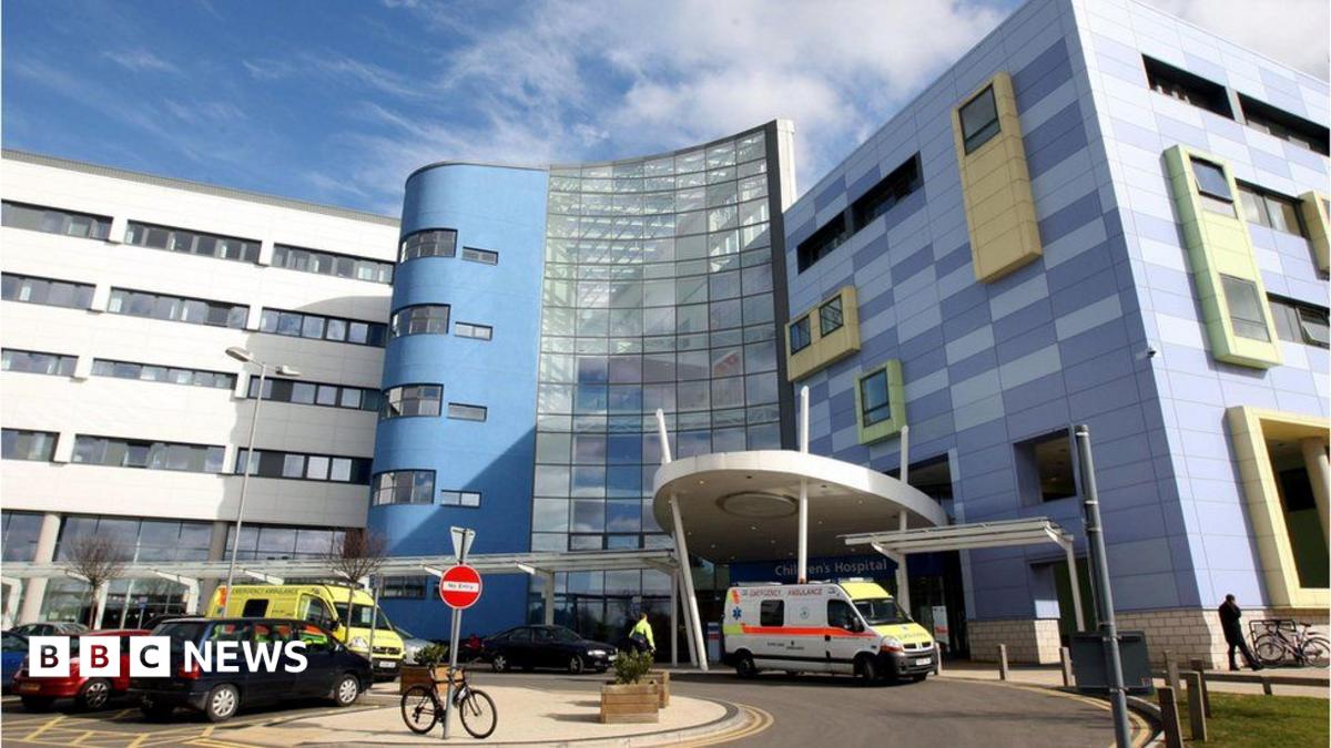 A picture of the John Radcliffe Hospital in Oxford. It is blue and grey, are there are cars and ambulances parked in front of it.