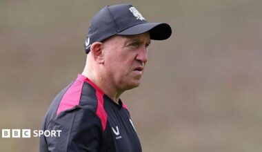 Shaun Edwards, wearing a black-and-red T-shirt and a black baseball cap, looks on during an England training session