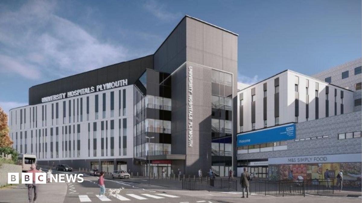 Modern hospital building exterior with multiple storeys, a central entrance tower, and people crossing the street in front. Visible signage reads “University Hospitals Plymouth” and “NHS”, under a clear blue sky.