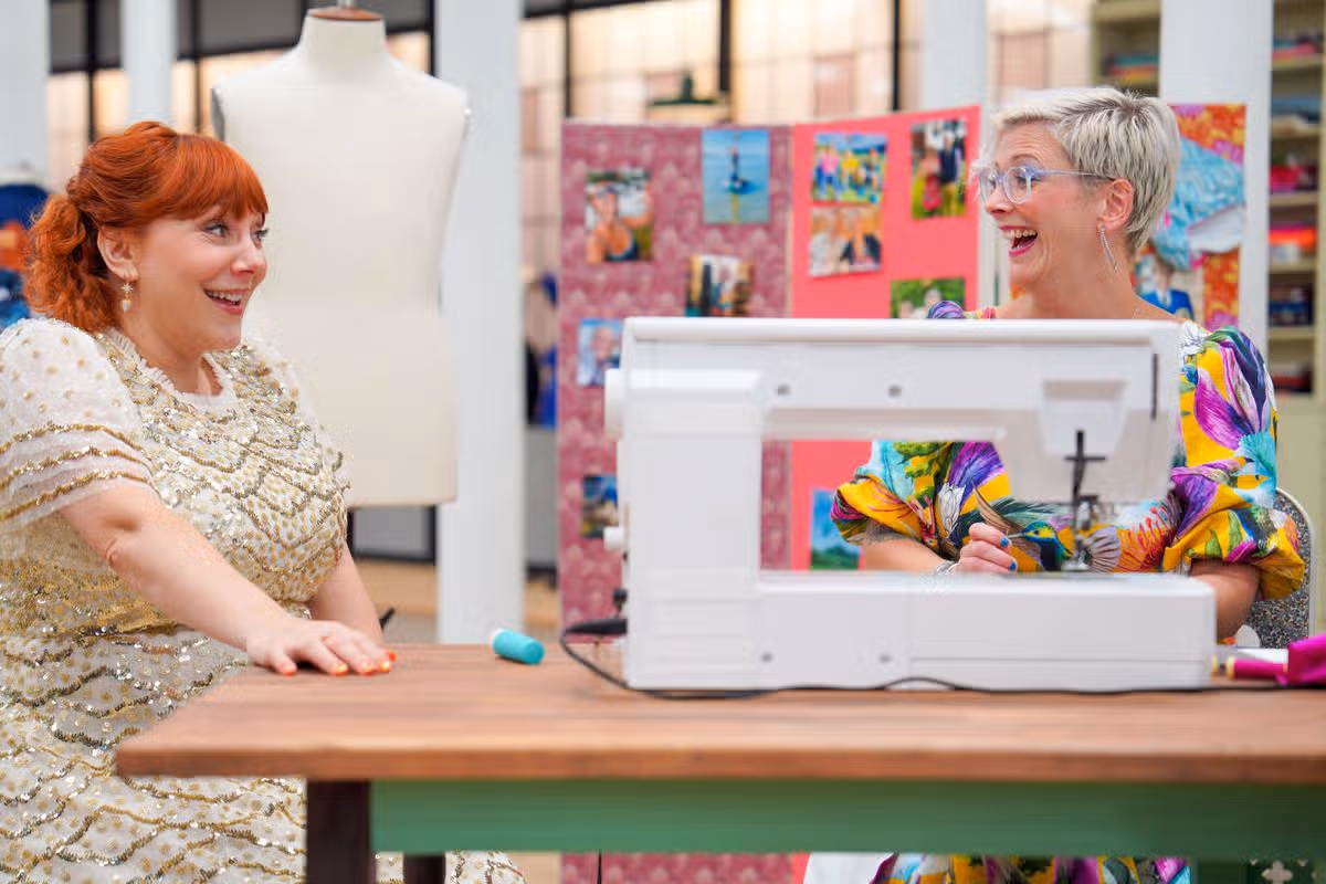 A woman in a sparkly dress speaking to someone sewing sat down