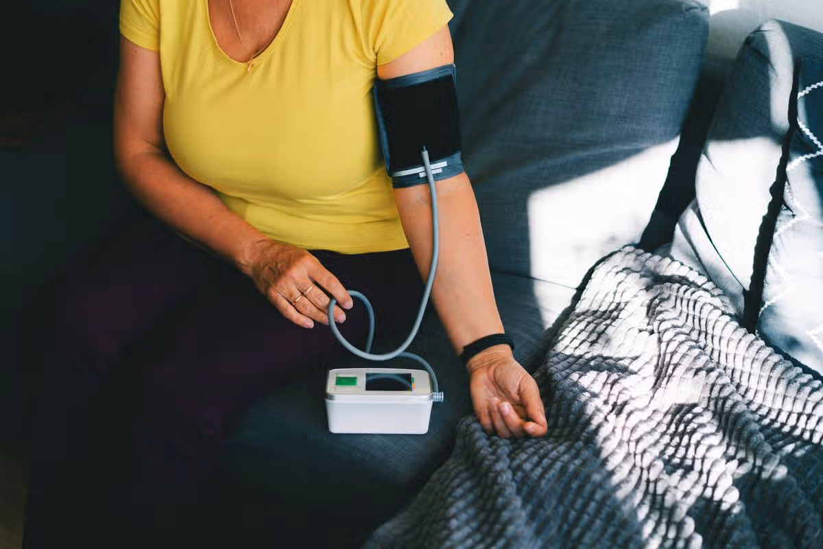 A close-up image of a person checking their blood pressure at home using a digital blood pressure monitor. The scene shows a relaxed individual seated on a cozy couch with a blood pressure cuff on their arm, illustrating the ease and convenience of home health monitoring. This image is ideal for conveying themes of health awareness, self-care, or medical technology in everyday life.