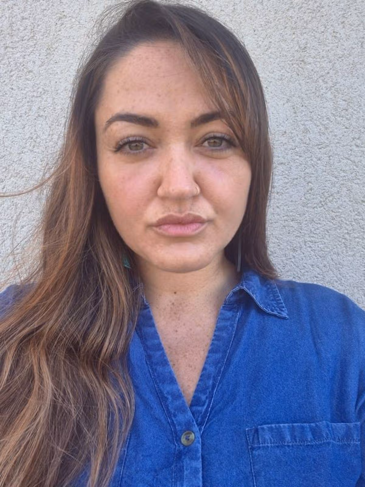 Nicole has fair skin and brown hair and is a young woman. She is wearing a royal blue collared shirt