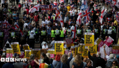 Protesters holding 'Stop the far right' posters with anti-migrant protesters waving St George and union flags on the steps beyond a line of police
