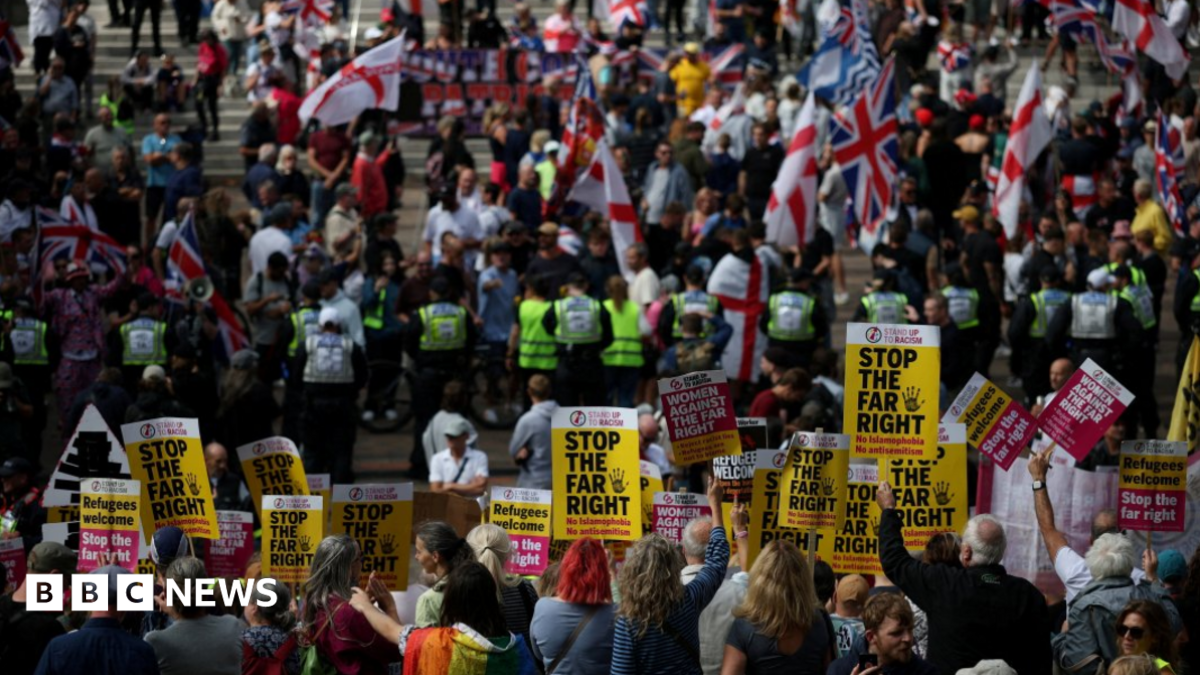 Protesters holding 'Stop the far right' posters with anti-migrant protesters waving St George and union flags on the steps beyond a line of police