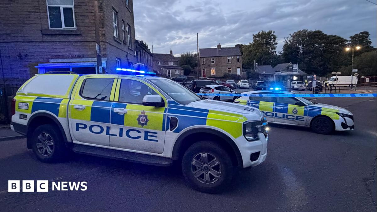 Two police cars with lights flashing parked alongside police cordon tape.