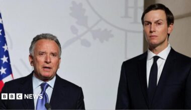 Steve Witkoff (left) and Jared Kushner (right) stand side by side looking directly towards the camera. They are both in black suits with white shirts. Witkoff has a blue patterned tie and Kushner has a black tie