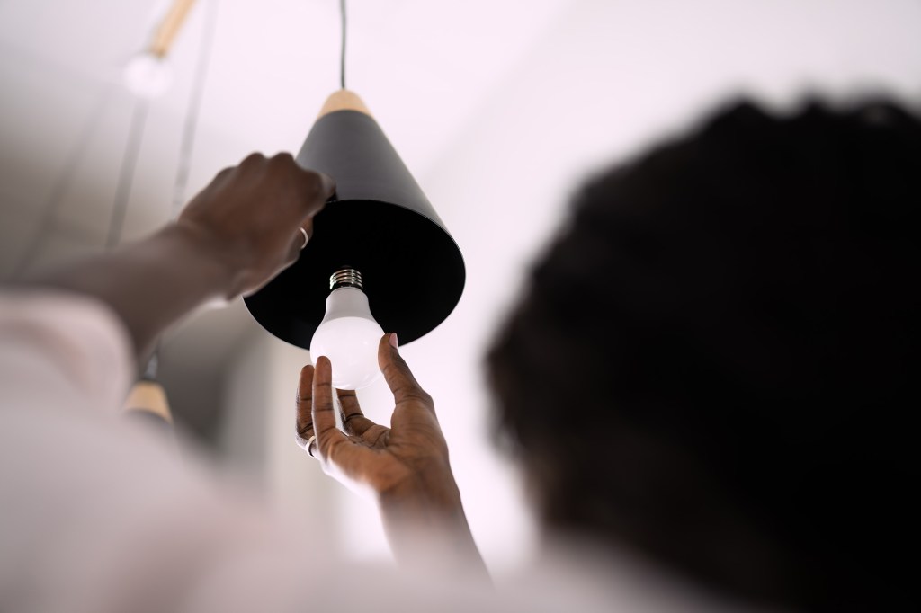 A person changes a lightbulb in a black hanging lamp.