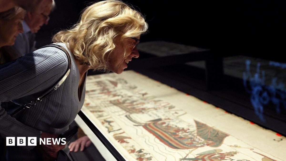 Shadowy figures of people viewing the Bayeux Tapestry up close
