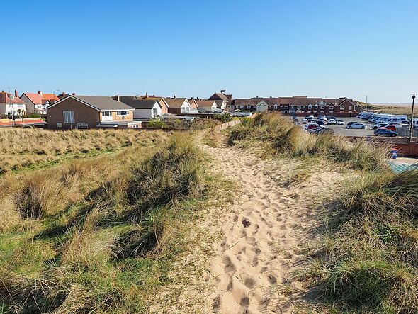 Lytham St Annes, Lancashire, Sandy path through coastal dunes leading to a residential area under a clear blue sky.