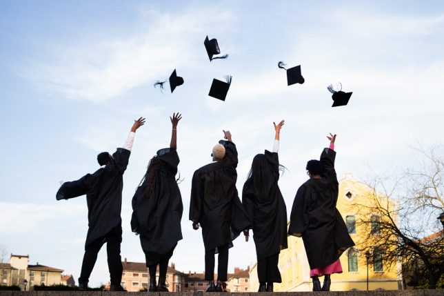 Young adults in graduation gowns joyfully tossing caps into the sky, celebrating achievement and new beginnings against a clear backdrop