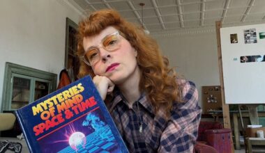 Melissa Auf Der Mar sits holding a book with her chin resting on her fist.