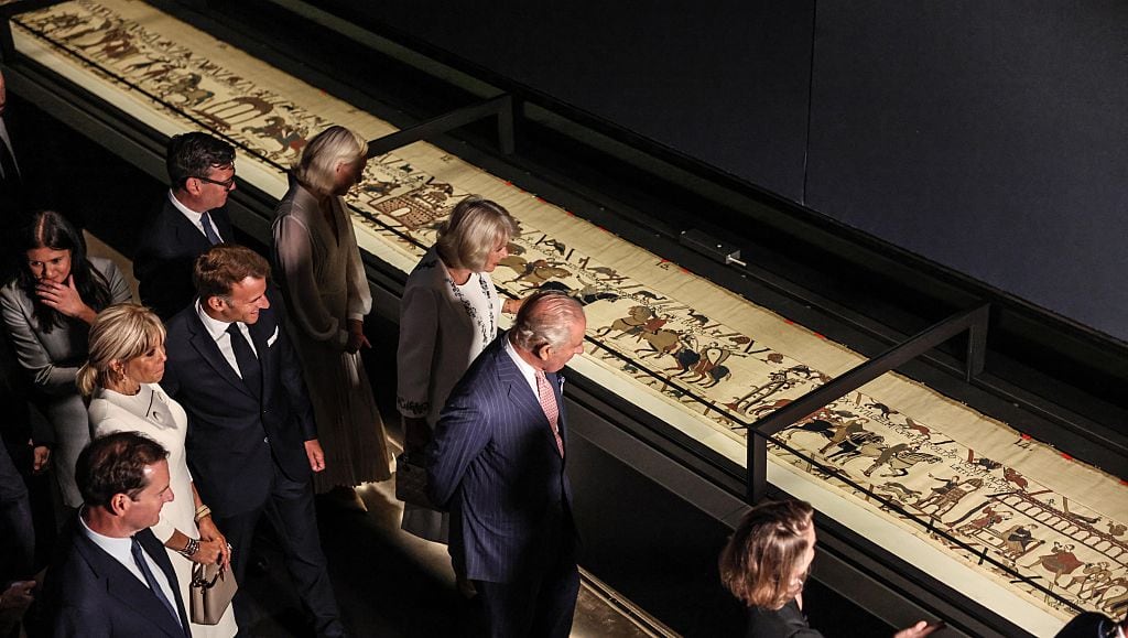 Several people look at a long tapestry in a display case.