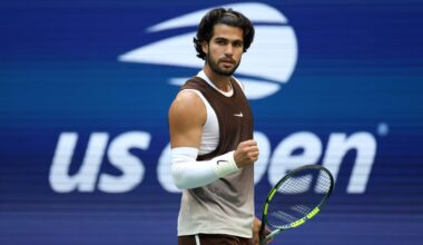 Tennis player in brown and white athletic wear, holding a racket, fist clenched, US Open background