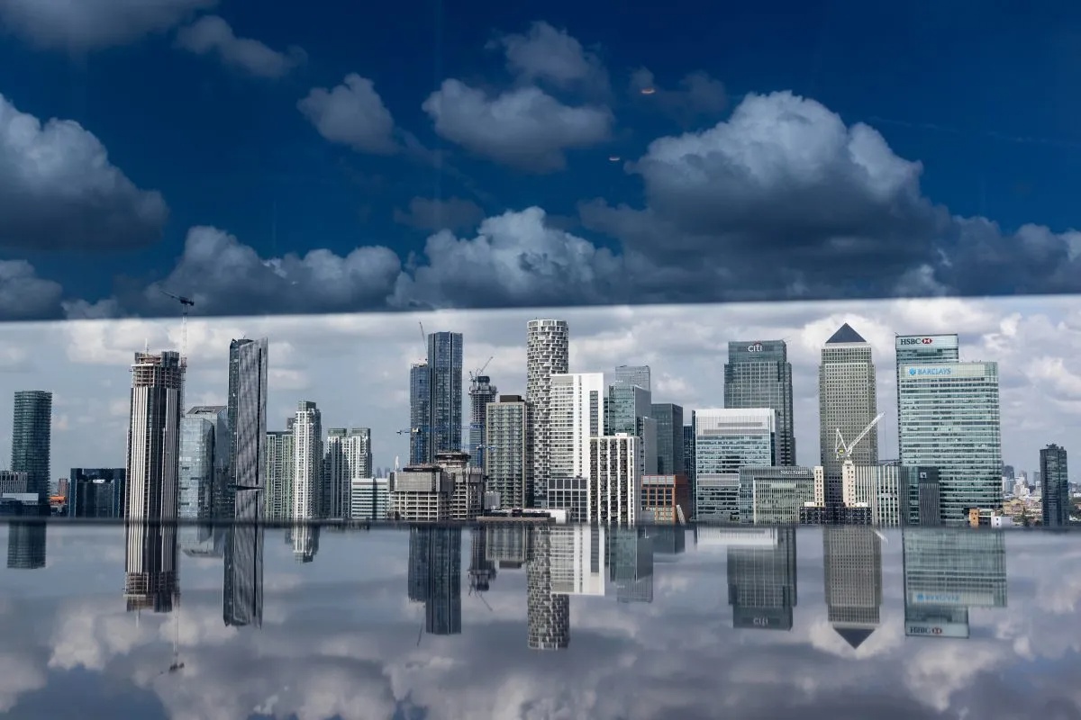 London financial district skyscrapers reflecting in water, under a dramatic cloudy sky