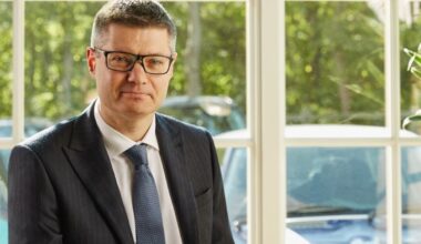 Simon Wolfson speaking at a business conference, wearing a suit and tie, addressing economic and retail industry topics