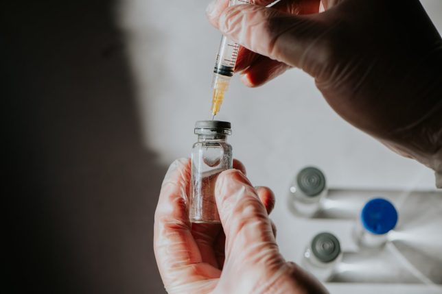 A healthcare professional uses a syringe to draw liquid medicine from a vial.