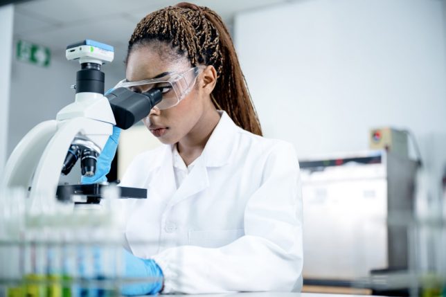 A female African-American scientist conducting and research on scientific sample though a microscope in a pharmaceutical laboratory.