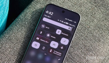 An Android smartphone resting on a textured fabric surface displaying the expanded Quick Settings shade with tiles for Wi-Fi, Bluetooth, Modes, and Battery Saver