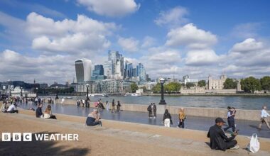 People sit in the autumn sunshine by the London Riverside in London