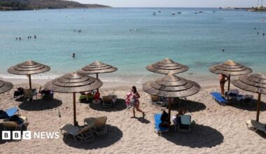 The beach with the sea in the background. There are sun beds and straw shades