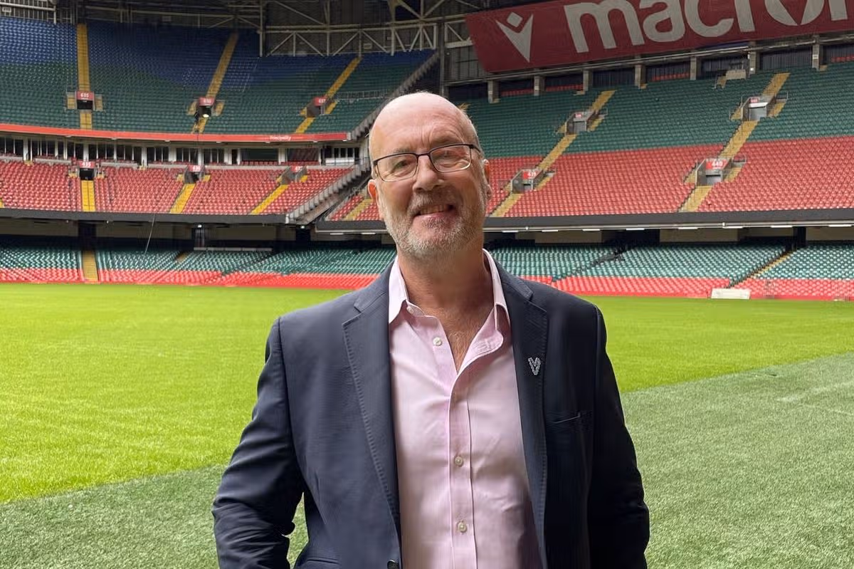 A smartly-dressed bald man stood on the pitch in an empty stadium