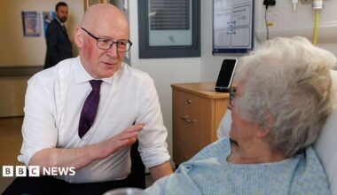 John Swinney talking to a female hospital patient who is in bed.