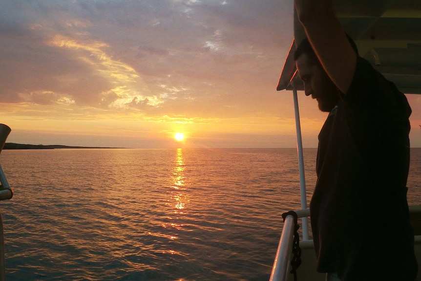A silhouette of a person on a boat with a sunset behind them over the water